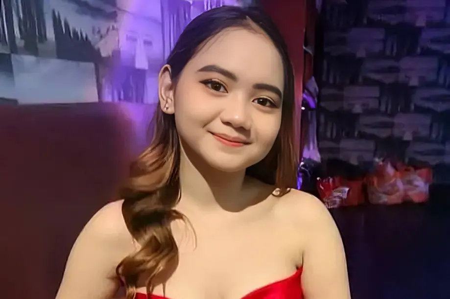 Mira, 18-year-old masseuse at PinkLady KL Sg Besi, smiling in red dress.